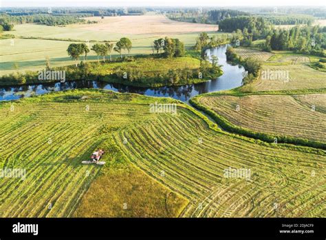 An aerial of a tractor cutting grass on a meadow next to a river during a beautiful summer ...