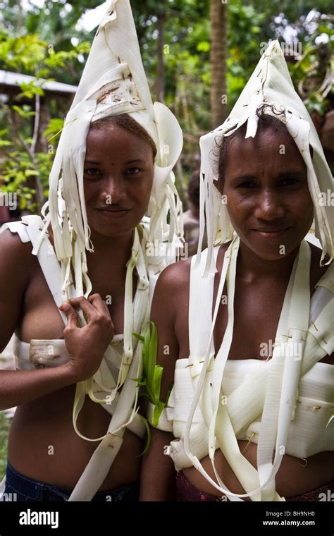 Two young Melanesian women wearing traditional white head dress and island costume smile into ...