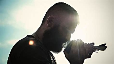 a man holding a bird in his right hand with the sun shining behind him on a sunny day