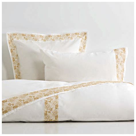a bed with white and gold pillows on top of it next to a pillow case