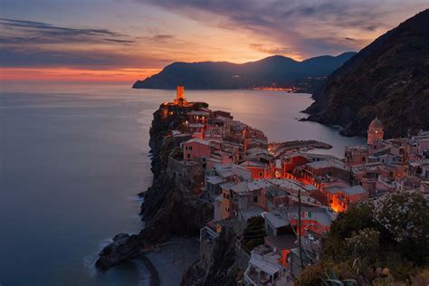 coastal town of vernazza in italy its buildings glowing orange as the sun sets behind a mountain ...