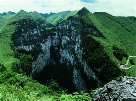 the mountains are covered with green vegetation and trees in the foreground is a large rock ...