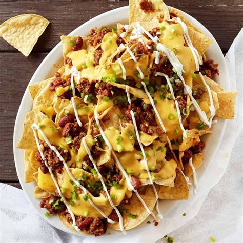 a white plate topped with nachos covered in cheese and sauce next to ...