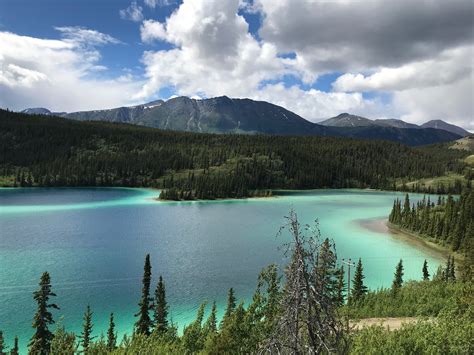 a lake surrounded by trees and mountains under a cloudy sky