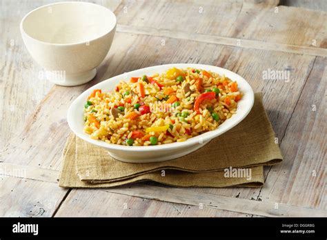 Savoury rice with, peas, red and yellow peppers, carrots and mushrooms in white serving dish ...