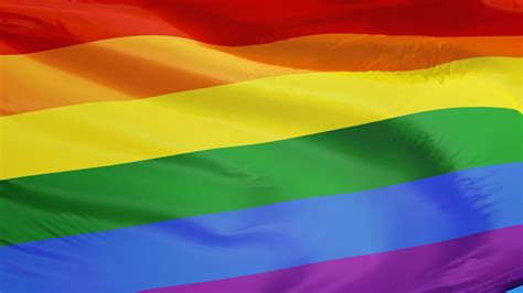 The gay pride rainbow flag waving against clean blue sky, close up, isolated with clipping path ...