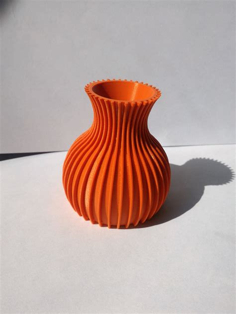 an orange vase sitting on top of a white table next to a shadow from the wall