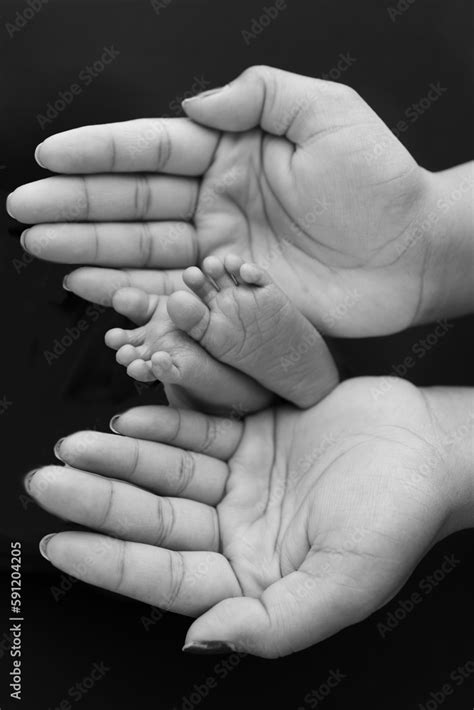 Black and white shade beautiful shape hands of mother, hold tiny newborn baby feet on black ...