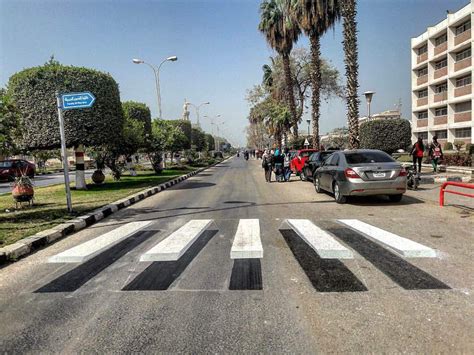 people are walking down the street in front of some palm trees and cars on the road