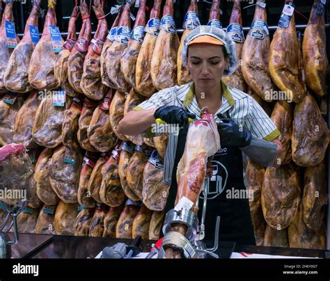 Woman carving Spanish Iberico ham with smoked ham legs hanging in ...