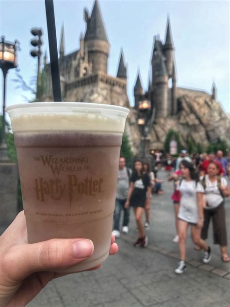 a person holding up a drink in front of hogwarts castle