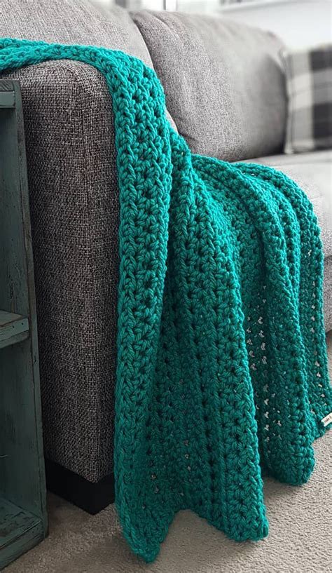 a green crocheted blanket sitting on top of a couch next to a book shelf