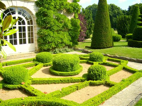 an outdoor garden with hedges and trees in the center, surrounded by stone walkways