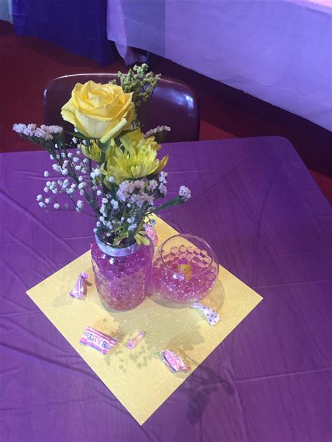 yellow roses and purple flowers are in a glass vase on a table with confetti