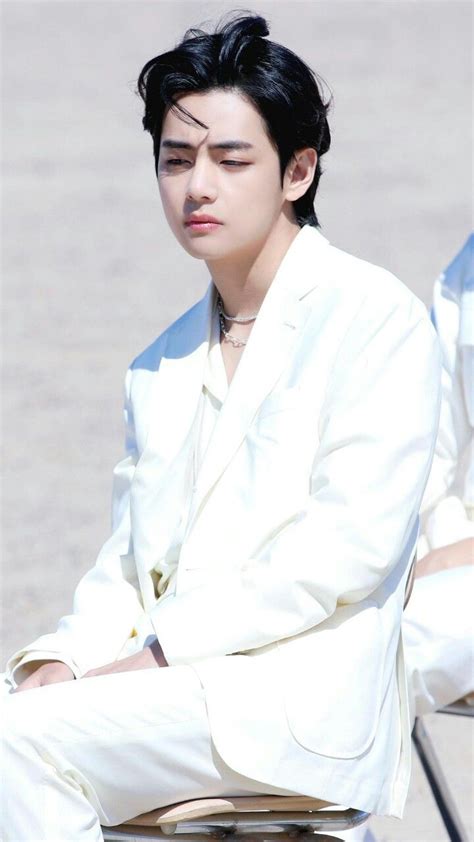 a young man sitting on top of a metal stool wearing a white suit and tie