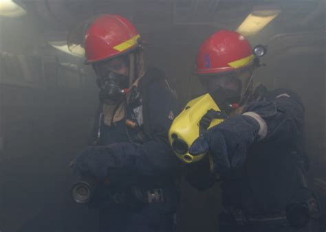 Sailor uses a Naval firefighter’s thermal imager to see through smoke as another holds a hose ...