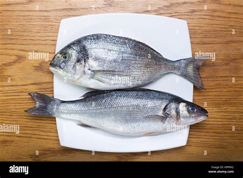 fresh raw fish sea bass and sea bream on a white plate on a wooden table Stock Photo - Alamy