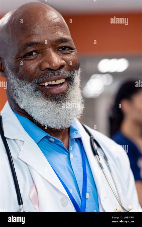 Vertical portrait of smiling senior male doctor with cancer ribbon in hospital ward, copy space ...