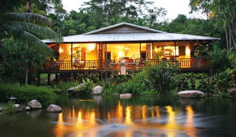 a house is lit up at night by the water's edge with trees around it