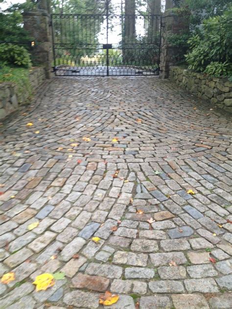 a cobblestone road with an iron gate at the end and trees in the background