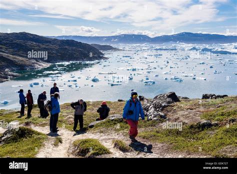 Hikers hiking on blue hike trail path by Jakobshavn or Ilulissat Icefjord with large icebergs in ...