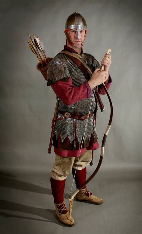 a man dressed in roman armor holding a bow and arrow while standing against a gray background