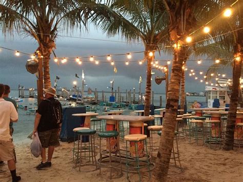 two men are standing on the beach near tables and chairs with lights strung from them