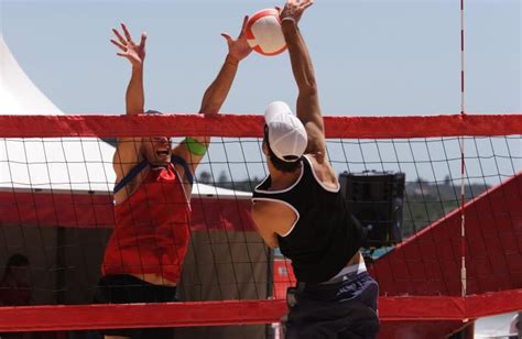 two people playing volleyball in front of a red net with the ball coming towards them