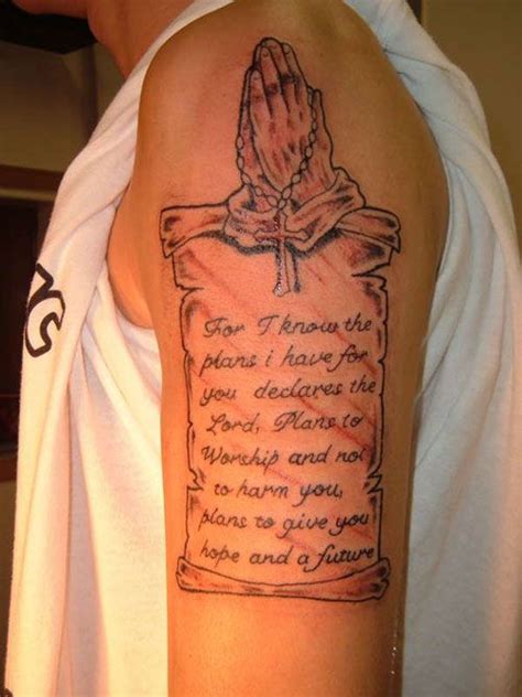 This scroll tattoo, etched on the arm, with folded hand and a rosary around it, expresses a ...