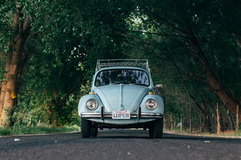 vintage blue volkswagen beetle parked on road in front of lake with mountains in the distance ...