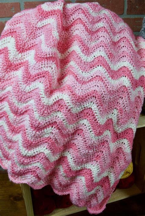 a pink and white crocheted blanket sitting on top of a wooden chair ...