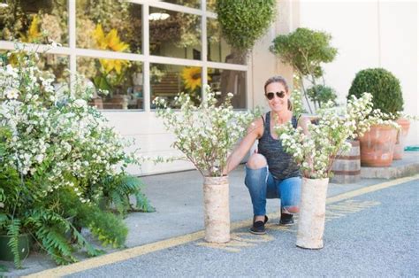 a woman kneeling down next to two tall vases with white flowers in front of a building