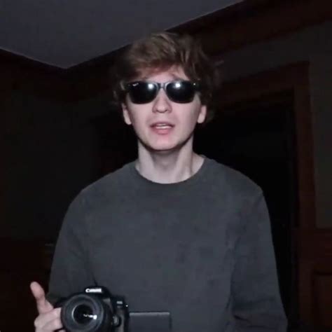 a young man wearing sunglasses and holding a camera in his right hand ...