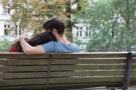 Young couple sitting on park bench, rear view - Stock Photo - Dissolve