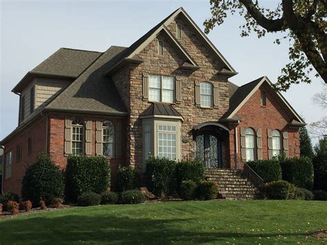 Red brick and stone combine with rock, taupe gray roof and shutters to create a modern country ...