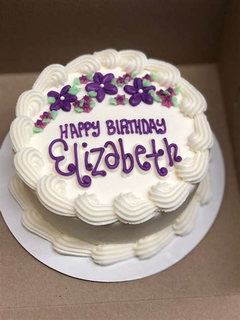 a birthday cake with white frosting and purple flowers on the top that ...