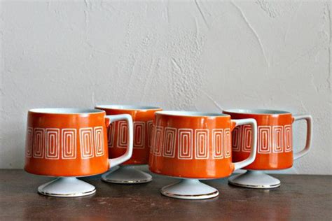 four orange and white coffee mugs sitting on top of a wooden table next to each other
