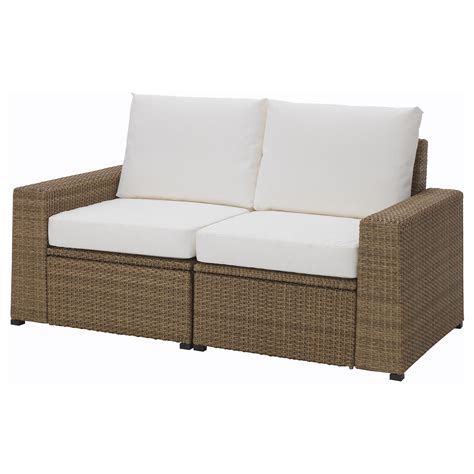 a brown wicker couch with two white pillows on the top and bottom cushions, facing each other