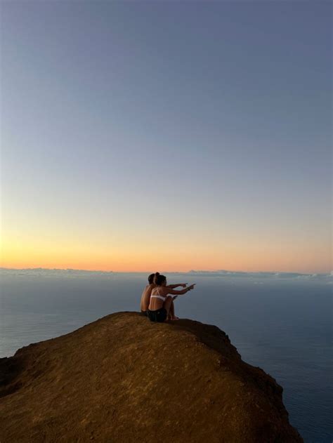 two people sitting on the edge of a cliff overlooking the ocean at ...