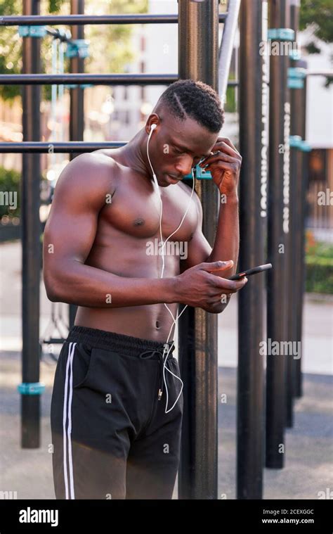 Muscular African American male athlete standing on sports ground and choosing tunes on ...