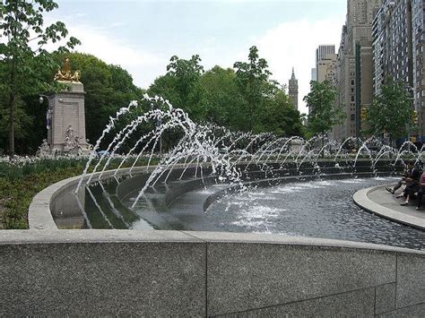 people sitting on benches next to a fountain with water spouting out of it