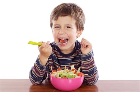 Niño comiendo ensalada a sobre fondo blanco | Foto Premium