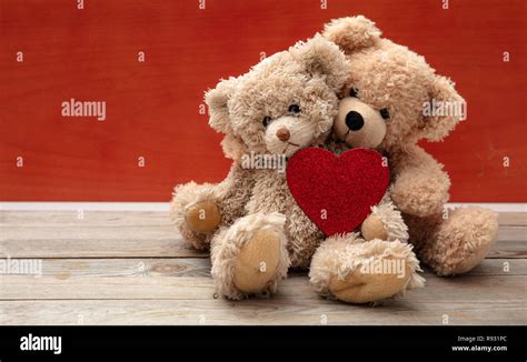 Love, friendship concept, tight hug. Two teddy bears embracing as a couple on wooden floor, red ...