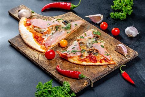 Ham pizza slices on an old wooden kitchen Board with tomatoes, chili and parsley - Creative ...