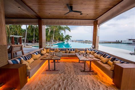 an outdoor living area with couches, tables and chairs on the sand near water