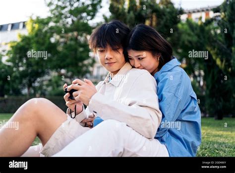 Cute asian couple sitting in the park together and using a camera Stock ...