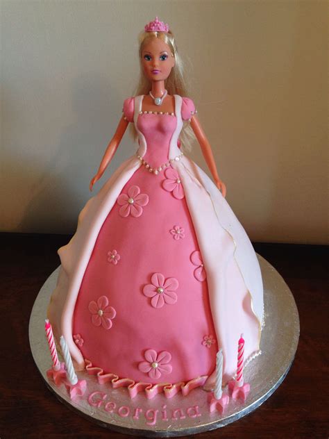 a barbie doll cake with pink and white frosting on it's side, sitting on a table