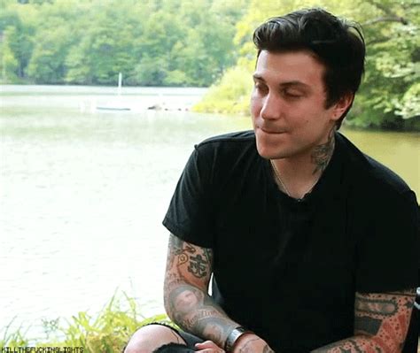 a man with tattoos sitting next to a lake