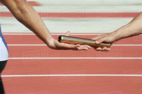 Runners exchanging baton in relay race, cropped - Stock Photo - Dissolve