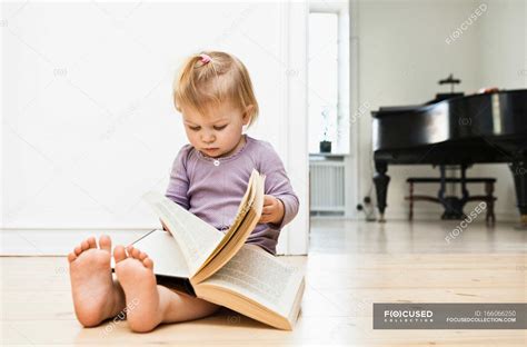 Toddler girl sitting on floor reading book — barefoot, only one girl ...